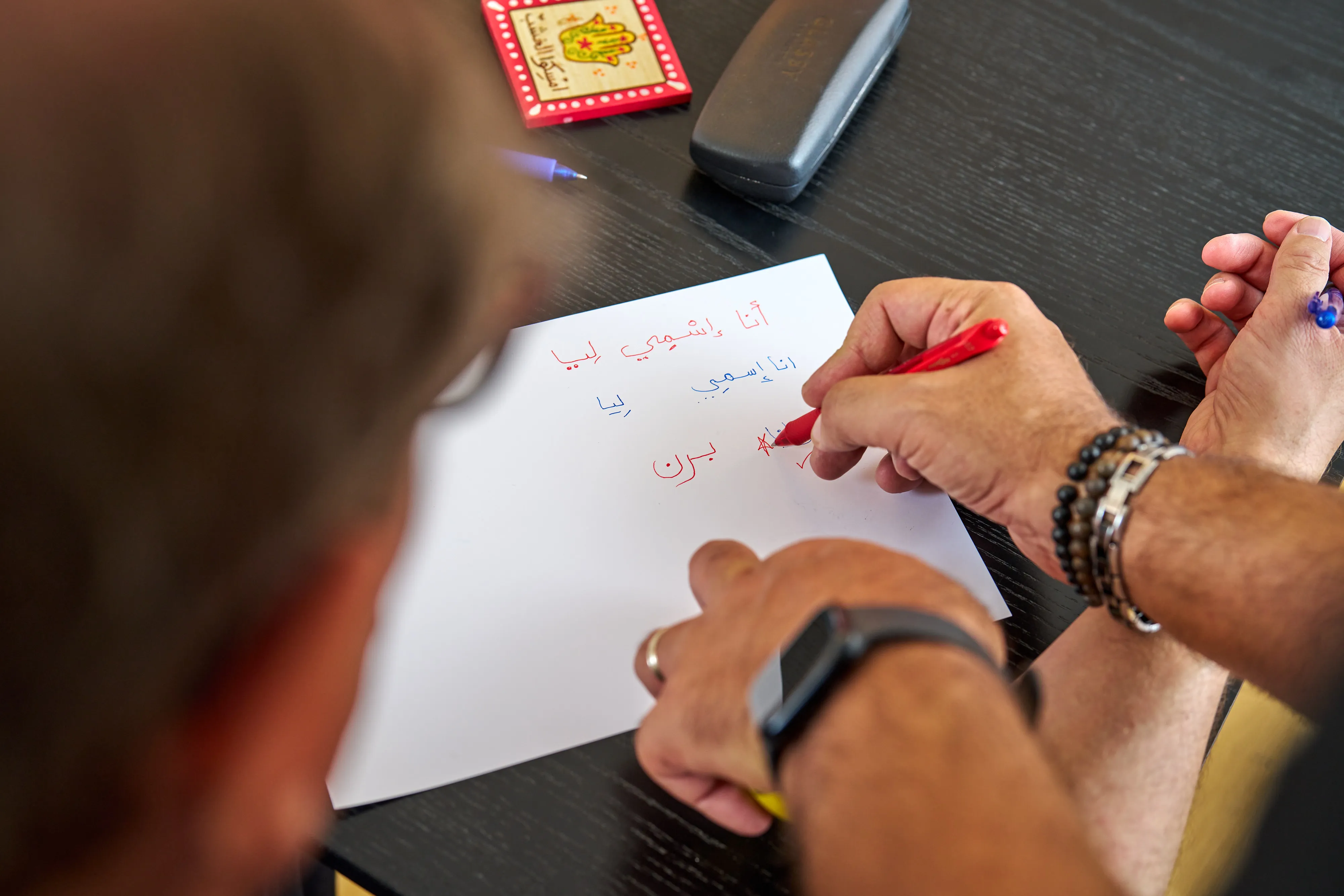 Hands writing Arabic sentences together during a lesson